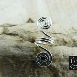 May include: Silver ear cuff with a spiral design. The cuff is made of wire and has a simple, elegant look.