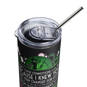 Op de afbeelding: Zwarte beker met een doorzichtig deksel en een zilveren rietje. De beker heeft een groen en zwart ontwerp met een heksensilhouet en de tekst "Don't cause commotions, I am on because I knew you have been changed for good."