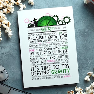 May include: A white rectangular print featuring a green clock graphic, a silhouette of a witch, and the text LESSONS THAT WICKED TAUGHT ME followed by various quotes including I AM ONE, CHANGED FOR GOOD, PINK GOES GOOD WITH GREEN, and DEFYING GRAVITY.