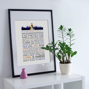 May include: A framed print with a white background and black frame. The print features a blue and gold design with the text "LESSONS THAT HAMILTON TAUGHT ME" and a list of quotes from the musical Hamilton.