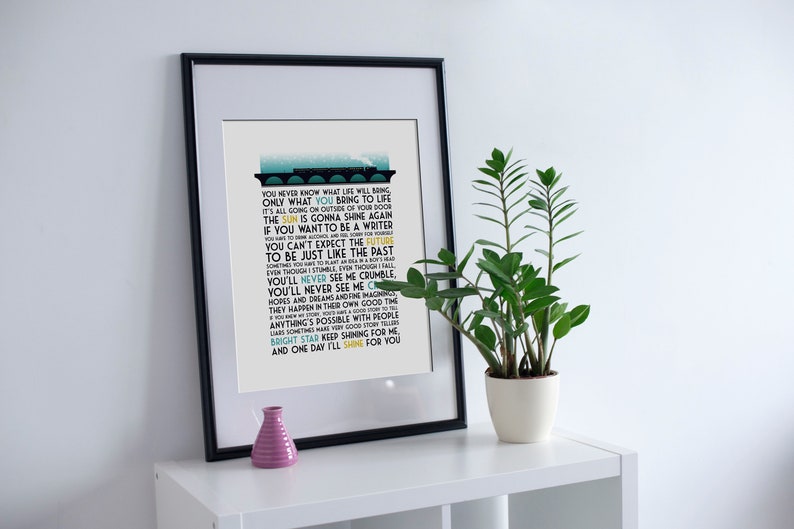 May include: A framed print with a black frame and a white background. The print features a blue and yellow graphic of a train with lyrics from the song "Bright Star" by Train. The lyrics include the words "You never know what life will bring, only what you bring to life."