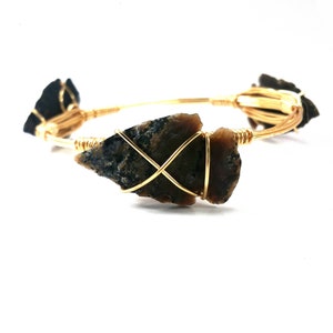 May include: A gold wire bangle bracelet with three brown and black arrowhead stones wrapped in wire.