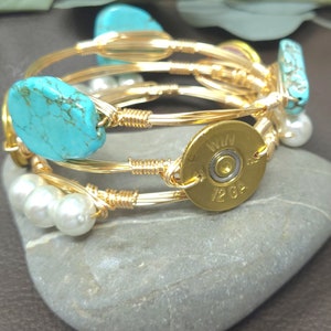 May include: Gold wire wrapped bangle bracelet with turquoise stones, pearls, and a brass bullet casing with the text "WIN 12 GA".
