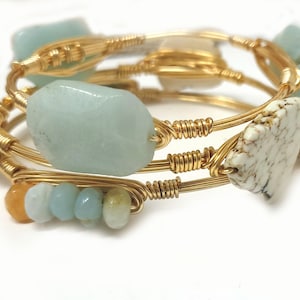 May include: Three gold wire wrapped bracelets with turquoise and white stones. The bracelets are stacked on top of each other.