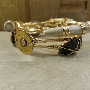 May include: A gold bangle bracelet with a white antler, a black stone, and a gold bullet casing charm.