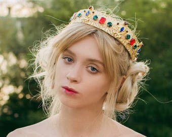 Könnte beinhalten: Eine junge Frau mit blonden Haaren trägt ein rotes, schulterfreies Kleid und eine goldene Krone mit bunten Juwelen.