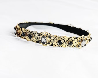 Könnte beinhalten: Ein goldenes Stirnband mit schwarzen und klaren Strasssteinen. Das Stirnband ist aus schwarzem Samt gefertigt und hat ein zartes Blumenmuster.