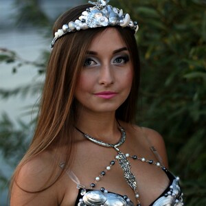 May include: A woman wearing a silver seashell crown and a black bra decorated with seashells and pearls.