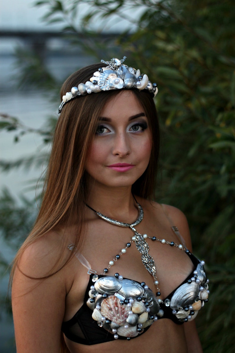 May include: A woman wearing a silver seashell crown and a black bra decorated with seashells and pearls.