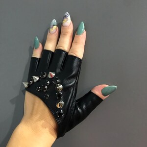 May include: Black leather fingerless gloves with silver studs and rhinestones. The gloves have a cut-out design on the back of the hand.
