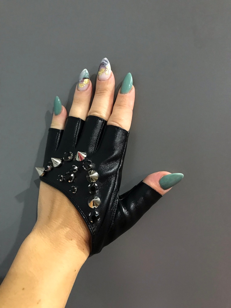 May include: Black leather fingerless gloves with silver studs and rhinestones. The gloves have a cut-out design on the back of the hand.
