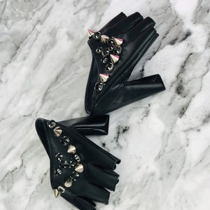 May include: A pair of black fingerless gloves with silver studs and rhinestones. The gloves are made of leather and have a pointed design.