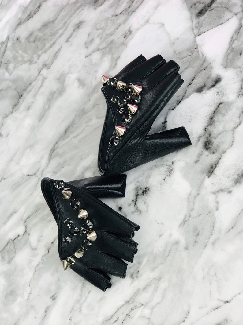 May include: A pair of black fingerless gloves with silver studs and rhinestones. The gloves are made of leather and have a pointed design.