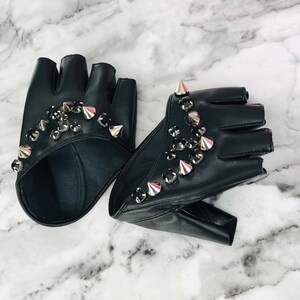 May include: A pair of black leather fingerless gloves with silver studs and rhinestones. The gloves are on a white marble surface.