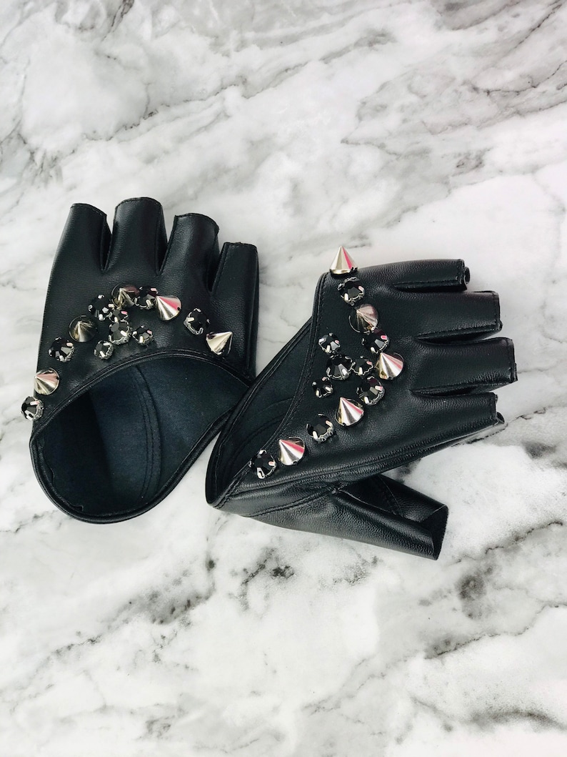 May include: A pair of black leather fingerless gloves with silver studs and rhinestones. The gloves are on a white marble surface.