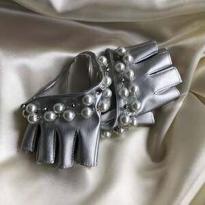 May include: A pair of silver leather fingerless gloves with a pearl and chain embellishment.