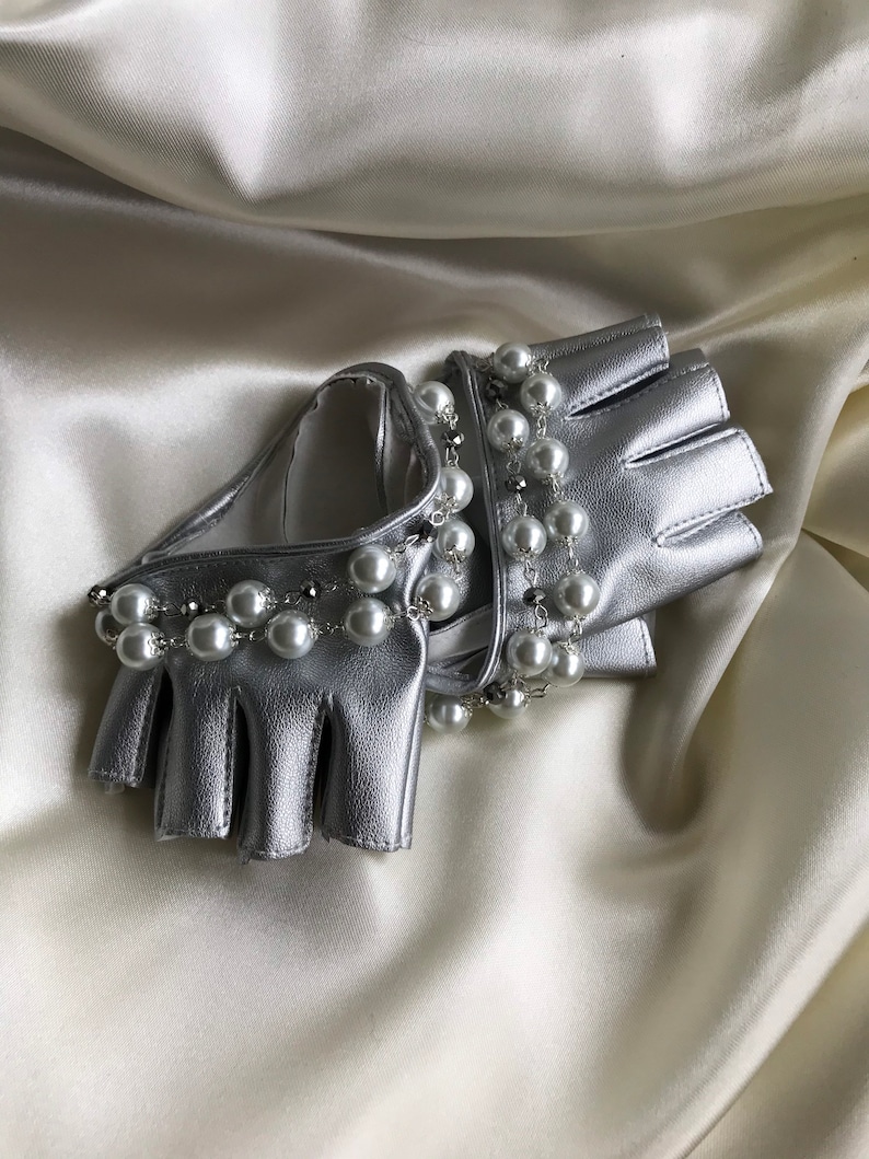 May include: A pair of silver leather fingerless gloves with a pearl and chain embellishment.