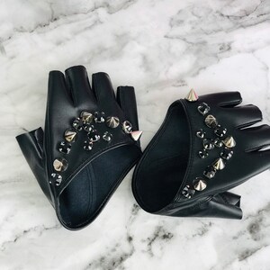 May include: A pair of black fingerless gloves with silver studs and black rhinestones. The gloves are made of leather and have a pointed design.