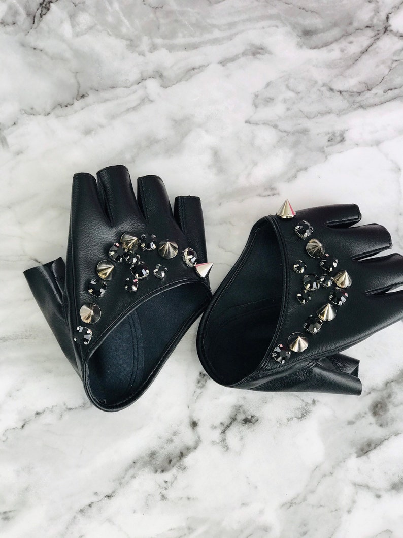 May include: A pair of black fingerless gloves with silver studs and black rhinestones. The gloves are made of leather and have a pointed design.