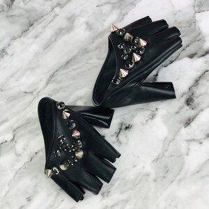 May include: A pair of black fingerless leather gloves with silver studs and rhinestones. The gloves are on a white marble surface.