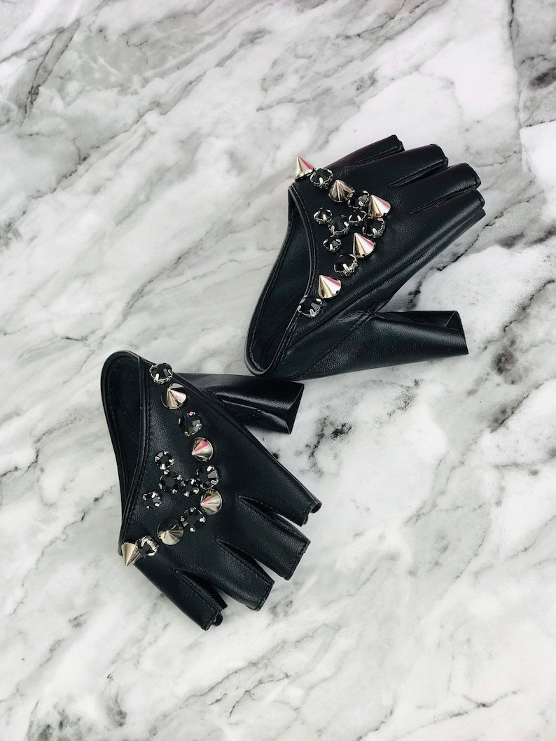 May include: A pair of black fingerless leather gloves with silver studs and rhinestones. The gloves are on a white marble surface.