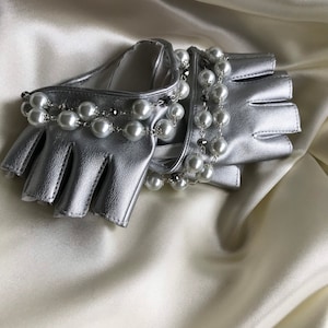 May include: Silver leather fingerless gloves with a pearl and chain embellishment.