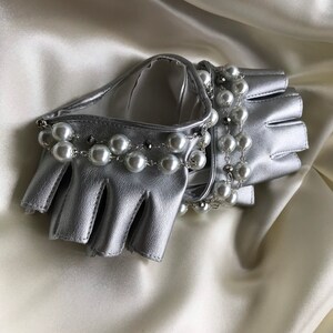 May include: Silver leather fingerless gloves with a pearl and chain embellishment.