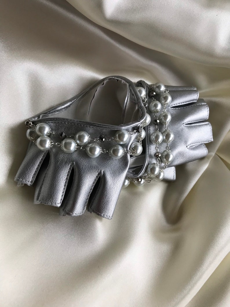 May include: Silver leather fingerless gloves with a pearl and chain embellishment.