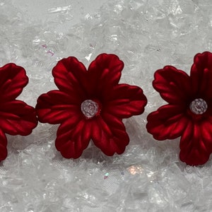 Puede incluir: Seis flores de tela roja con un centro de purpurina plateada. Las flores están dispuestas en una fila sobre un fondo blanco.