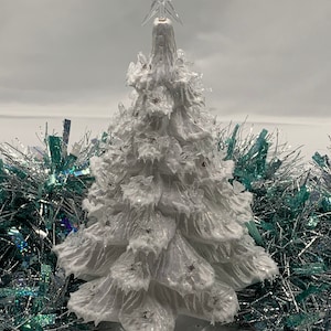 Può includere: Un albero di Natale bianco ghiacciato con una stella in cima. L'albero è circondato da festoni argentati e turchesi.