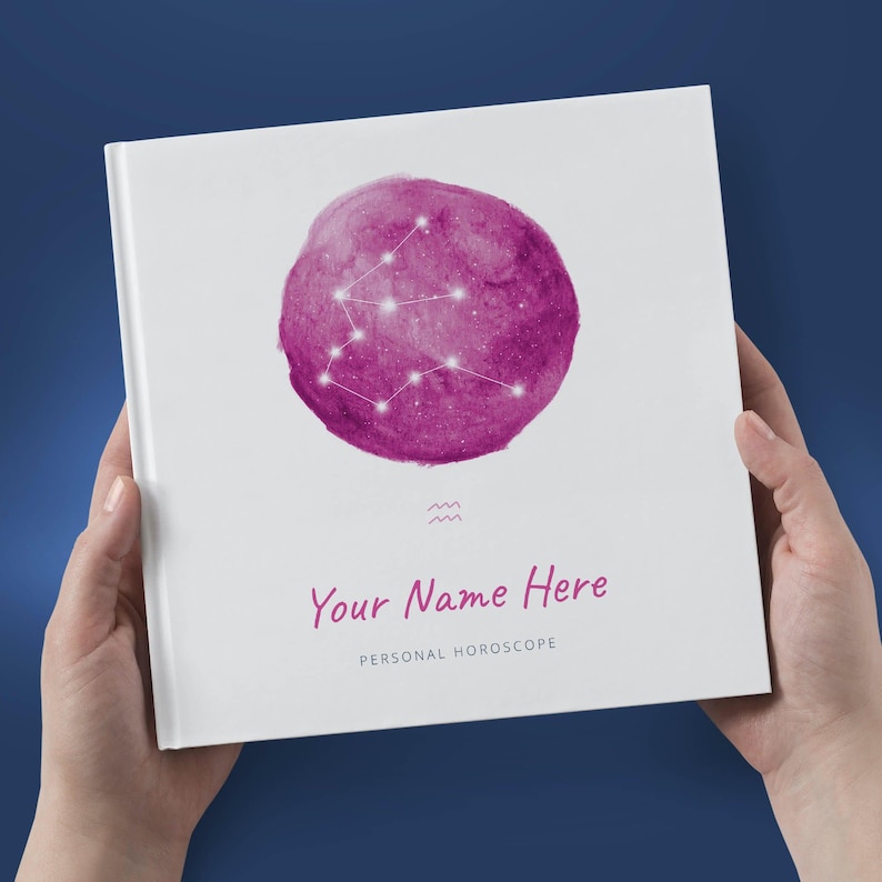 May include: A white book with a pink watercolor circle featuring the Aquarius constellation. The text "Your Name Here" and "Personal Horoscope" is printed on the front cover.