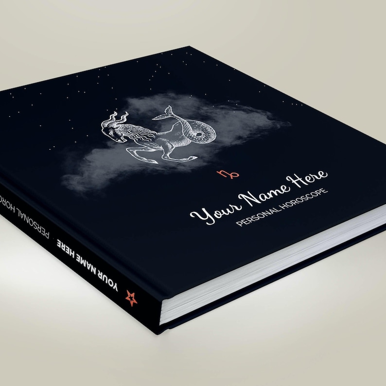 May include: A black book with a white illustration of the Capricorn zodiac sign on a dark blue background with white stars. The book has the text "Your Name Here" and "Personal Horoscope" on the cover.