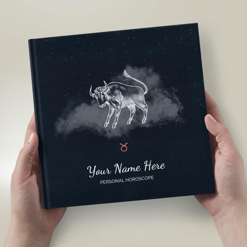 May include: A black hardback book with a white illustration of a bull against a dark blue starry sky background. The book has the text "Your Name Here PERSONAL HOROSCOPE" printed on the front cover.