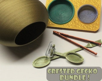 May include: Crested Gecko Bundle!  A set of reptile care items including a green and yellow patterned dish, a brown and green patterned dish, a brown and orange pair of tongs, a green and brown patterned dish with a clear suction cup, and a brown ceramic hide.