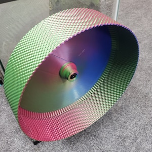 Peut inclure: Une roue d'exercice circulaire pour petits animaux présentant un dégradé de couleurs irisé et vibrant passant du vert au bleu et au magenta. La surface extérieure possède une texture en losanges, tandis que l'intérieur est lisse.