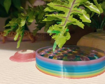 Puede incluir: Un juguete de plástico circular de varios niveles con colores arcoíris. El juguete está hecho de varias capas delgadas y flexibles de plástico, cada capa de un color diferente del arcoíris. El juguete está sobre una superficie blanca.