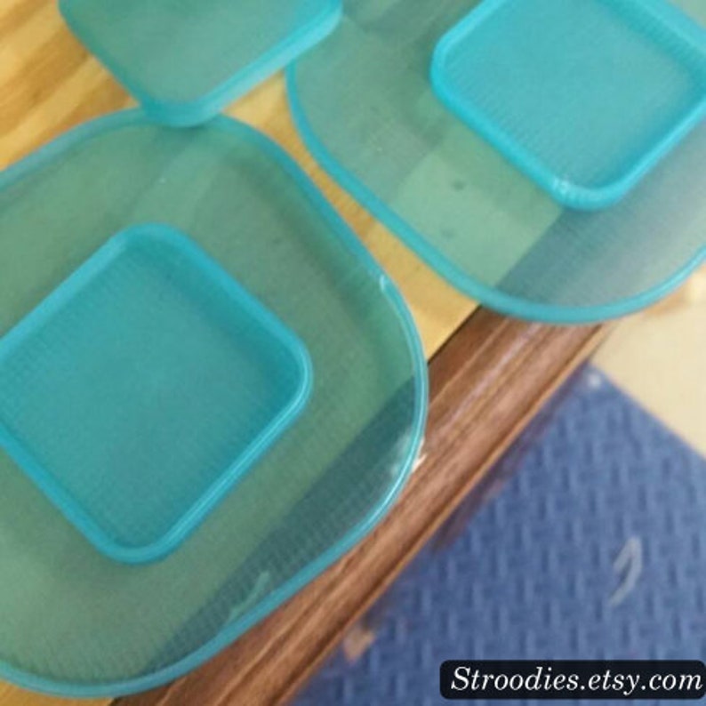 May include: Four turquoise blue plastic trays with a square shape in the center of each tray. The trays are stacked on top of each other.