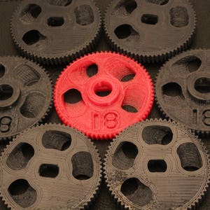 May include: A set of eight gears, seven are black and one is red. The red gear has the number "18" printed on it.