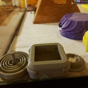K&ouml;nnte beinhalten: Drei 3D-gedruckte Reptilien-Gehege, eines ist eine quadratische Box mit Deckel, eines ist eine runde Schale mit einem Mittelpfosten und das andere ist eine runde Schale mit einem erh&ouml;hten Rand.