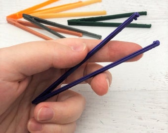 May include: A set of colorful plastic tweezers, with one pair of purple tweezers held in a hand. The tweezers are designed for crafts and small tasks.