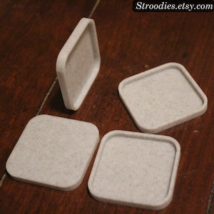 May include: Four square white coasters with a speckled texture. The coasters are made of a durable material and are perfect for protecting surfaces from scratches and spills.