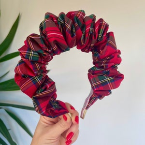 May include: A red plaid headband with a ruffled design. The headband features a classic tartan pattern in red, green, yellow, and brown. The fabric is gathered and sewn onto a sturdy base, creating a voluminous, stylish accessory.