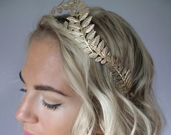 May include: A woman with blonde hair is wearing a gold leaf headband. She is wearing a pink and black leopard print shirt.