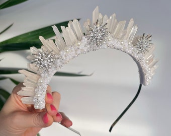 May include: A white crystal headband with silver star accents and pearl beads. The headband is made of a flexible metal and is designed to fit comfortably on the head.