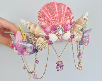 May include: A pink and white seashell crown with pink and purple beads, gold chains, and a pink crystal pendant.