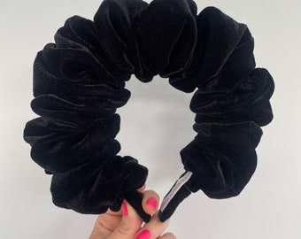 May include: Black velvet scrunchie with a gathered, ruffled design. The scrunchie is made of soft, plush velvet and has a simple, elegant look.