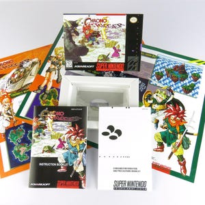 Peut inclure: Un coffret de jeu vidéo Chrono Trigger pour Super Nintendo. La boîte est ouverte, révélant la cartouche de jeu et divers encarts. L'illustration de la boîte présente des illustrations colorées de personnages et le titre du jeu.