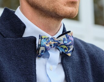 May include: A man wearing a navy blue blazer with a white shirt and a colorful bow tie with a pattern of animals.