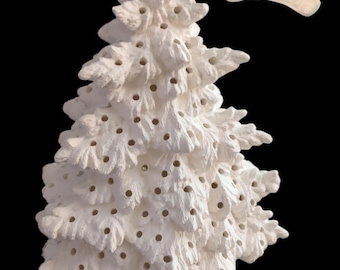 May include: A white ceramic Christmas tree with numerous small holes for lights. The tree has a textured surface and a separate, matching base. The background is black.