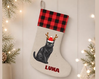 Peut inclure: Une chaussette de Noël beige avec un revers à carreaux rouges et noirs. Au centre, une illustration représente un chat noir portant un bonnet de Père Noël rouge avec des bois de renne bruns. Le nom LUNA est inscrit en lettres à carreaux.
